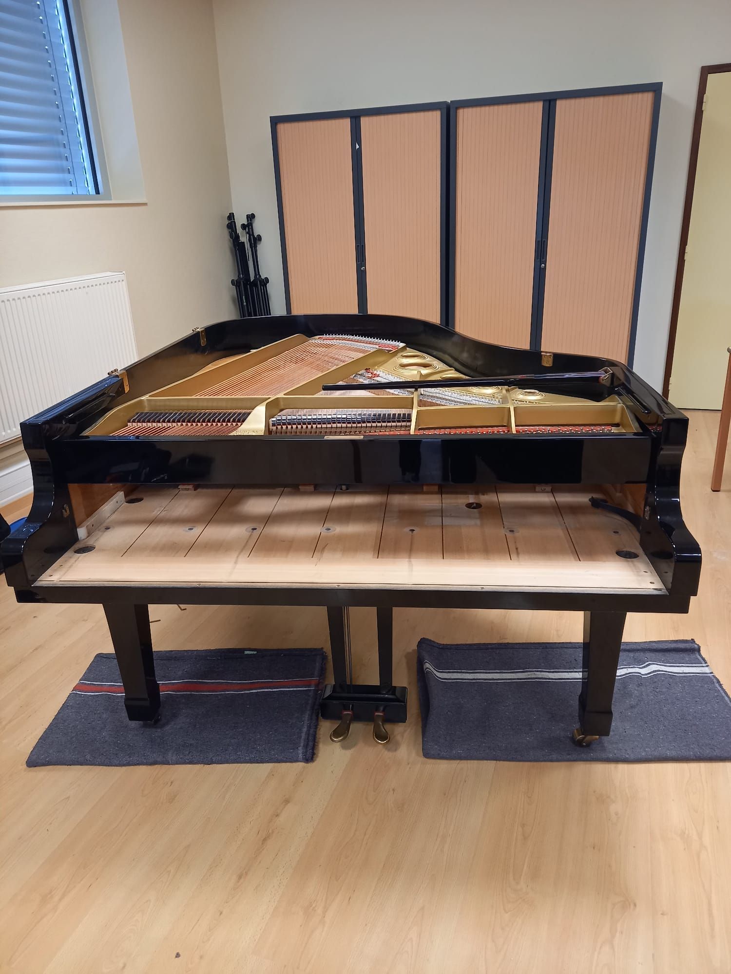 Piano à queue, couvercle ouvert, dans une pièce, laissant apparaître les cordes et le cadre en bois.