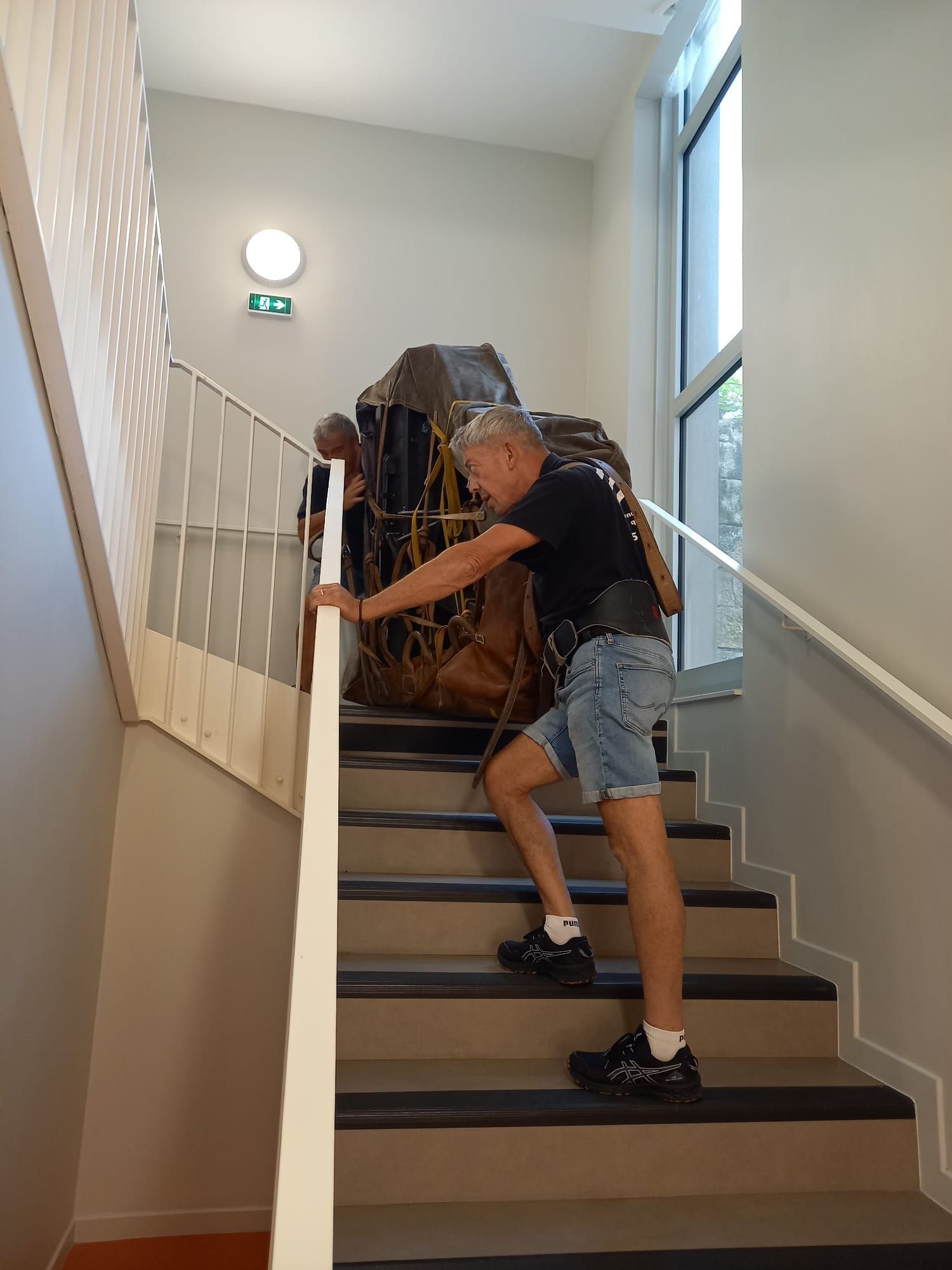 Une personne transportant un gros paquet dans un escalier intérieur d'un couloir lumineux.