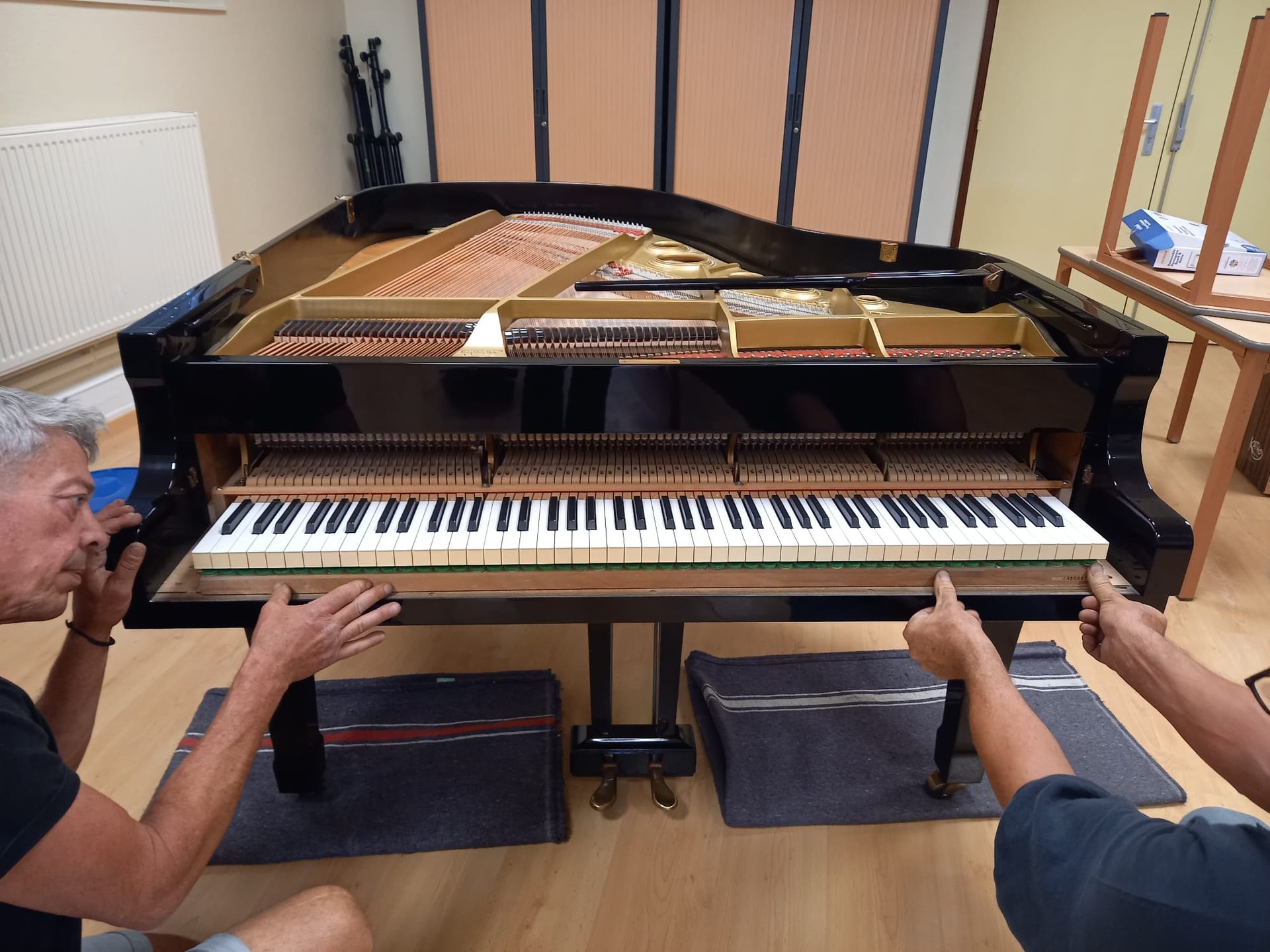 Des hommes règlent un piano à queue dans une pièce, le couvercle ouvert et son intérieur visible.