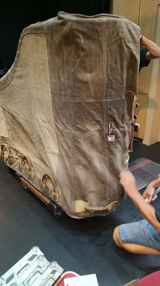 Machine de grande taille, recouverte et montée sur un socle à roulettes, en cours de réglage par une personne dans un atelier.