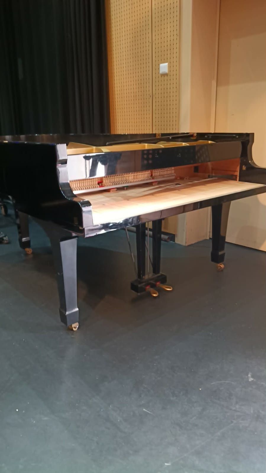 Un piano à queue noir sur une scène avec un banc dans une pièce lambrissée.