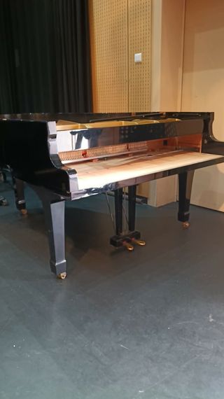 Un piano à queue noir sur une scène aux rideaux sombres et aux panneaux muraux en bois.