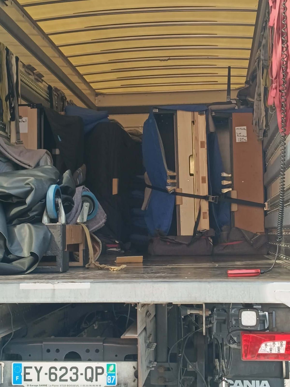 Camionnette ouverte avec des meubles emballés, des sacs et une plaque d'immatriculation visible sur le pare-chocs arrière.