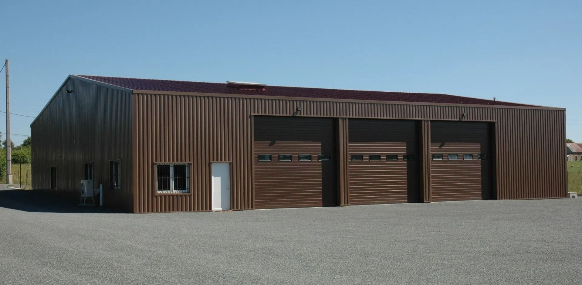 Bâtiment de garage en métal brun avec trois portes sectionnelles sur un terrain en gravier