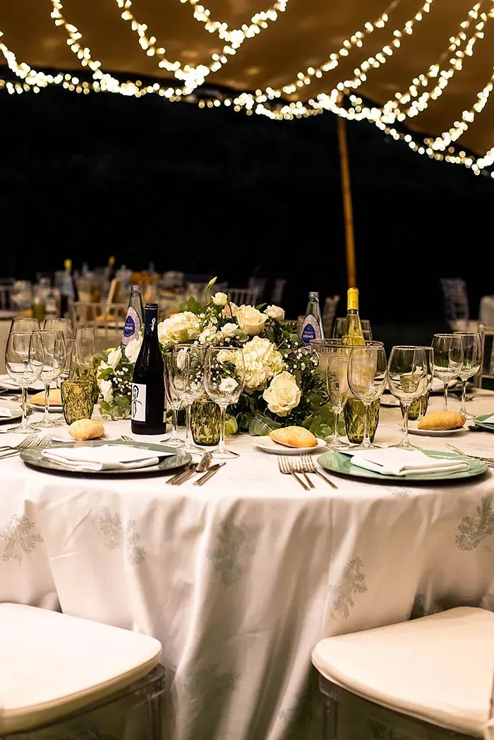 Una mesa puesta para una recepción de boda bajo una carpa con una botella de vino sobre ella.