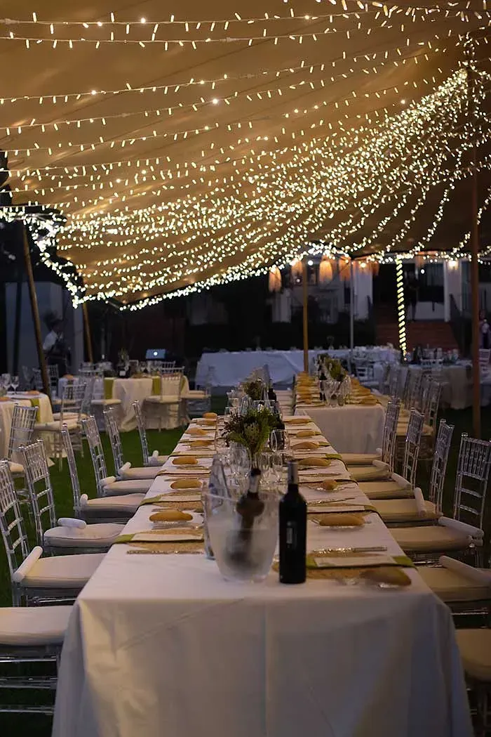 Una mesa larga con una botella de vino encima, debajo de una carpa.