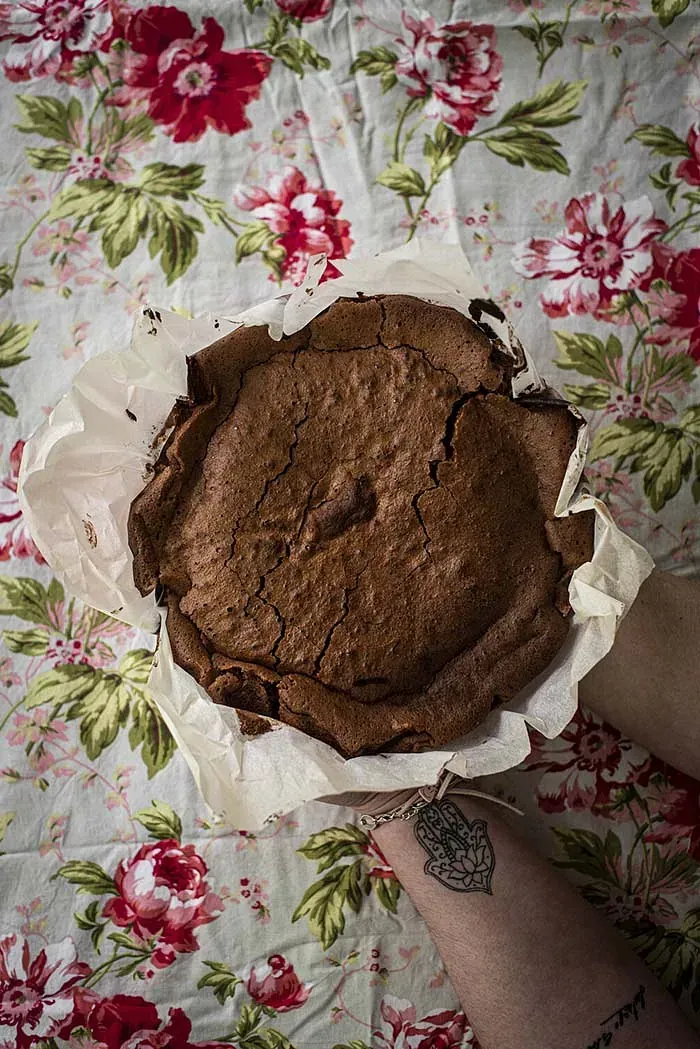Una persona sostiene un pastel de chocolate sobre un mantel floral.