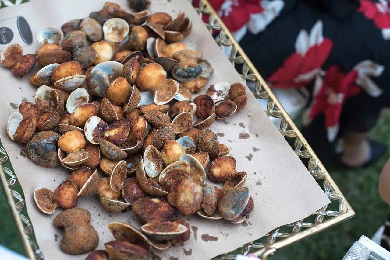 Una persona sostiene una bandeja de almejas fritas sobre una mesa.