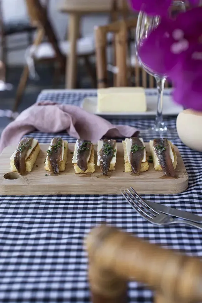 Una tabla de cortar de madera con sándwiches sobre un mantel a cuadros.