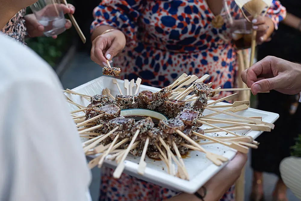 Un grupo de personas está comiendo brochetas de carne en un plato.