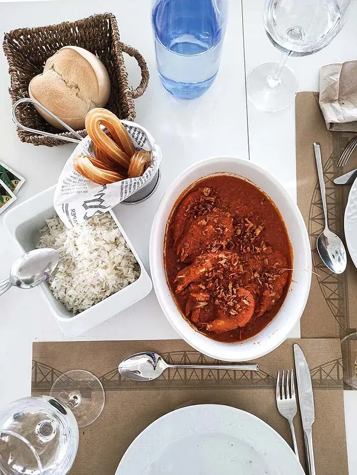 Una mesa con platos, cubiertos, un cuenco de comida y una cesta de pan.