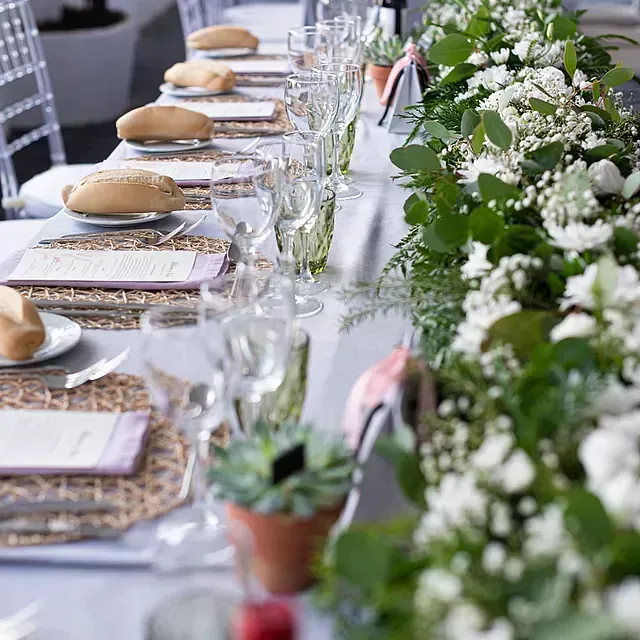 Una mesa larga con platos, vasos y flores sobre ella.