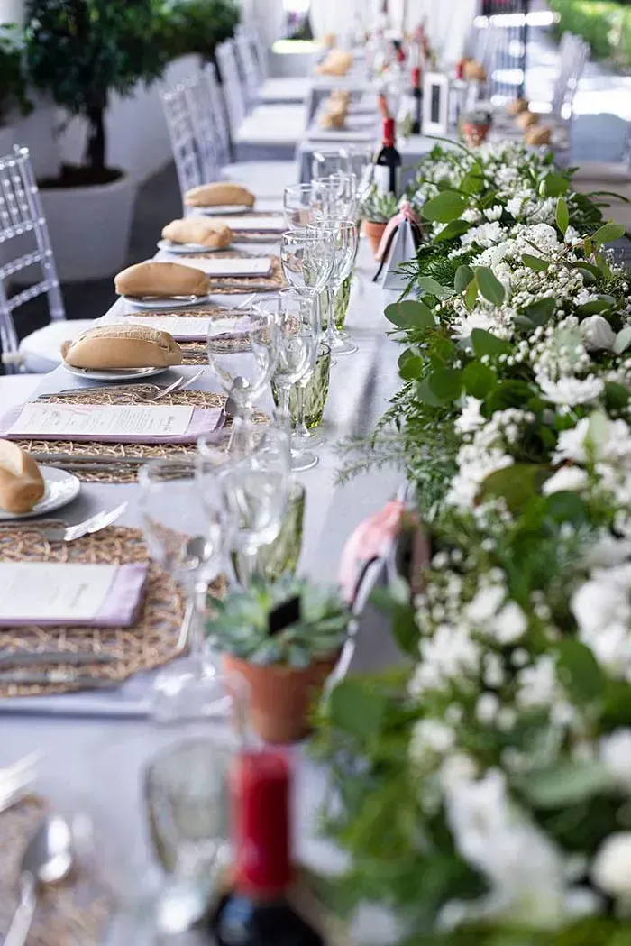 Una mesa larga con platos, vasos y flores sobre ella.