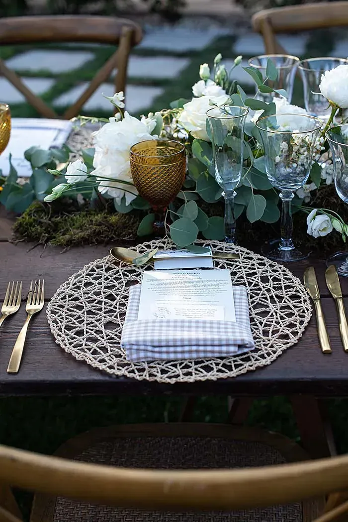 Una mesa preparada para una recepción de boda con flores y utensilios sobre ella.