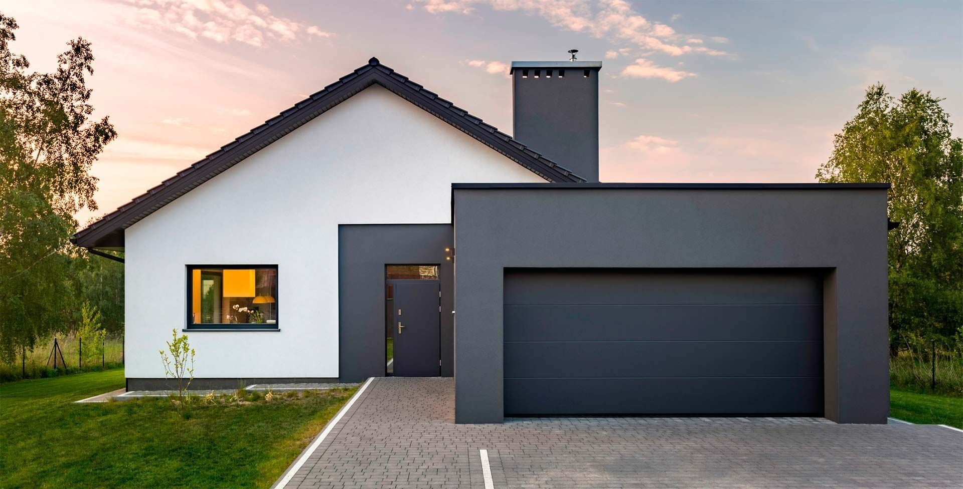 Casa moderna de color blanco y gris oscuro con garaje, chimenea y entrada pavimentada.
