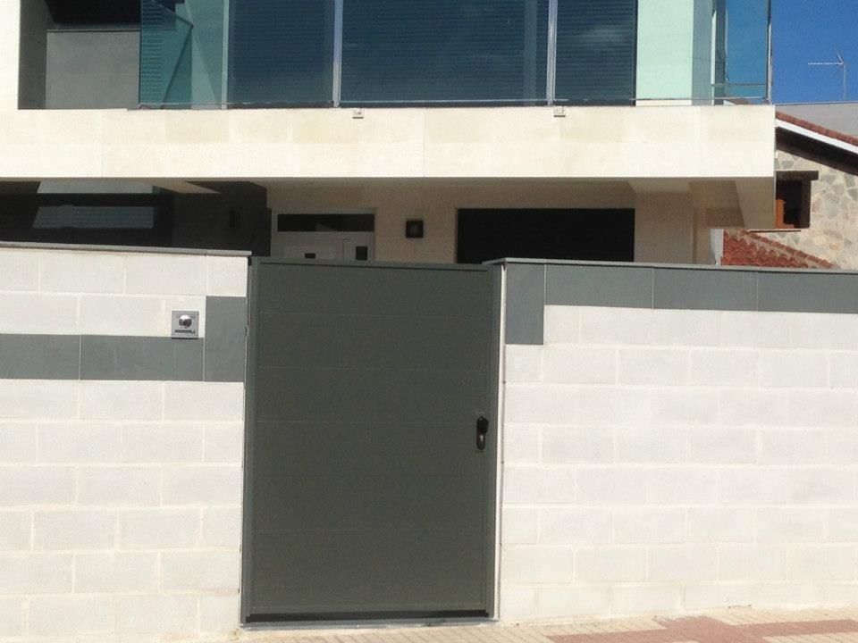 Puerta gris frente a un moderno edificio de dos pisos con balcón de vidrio.