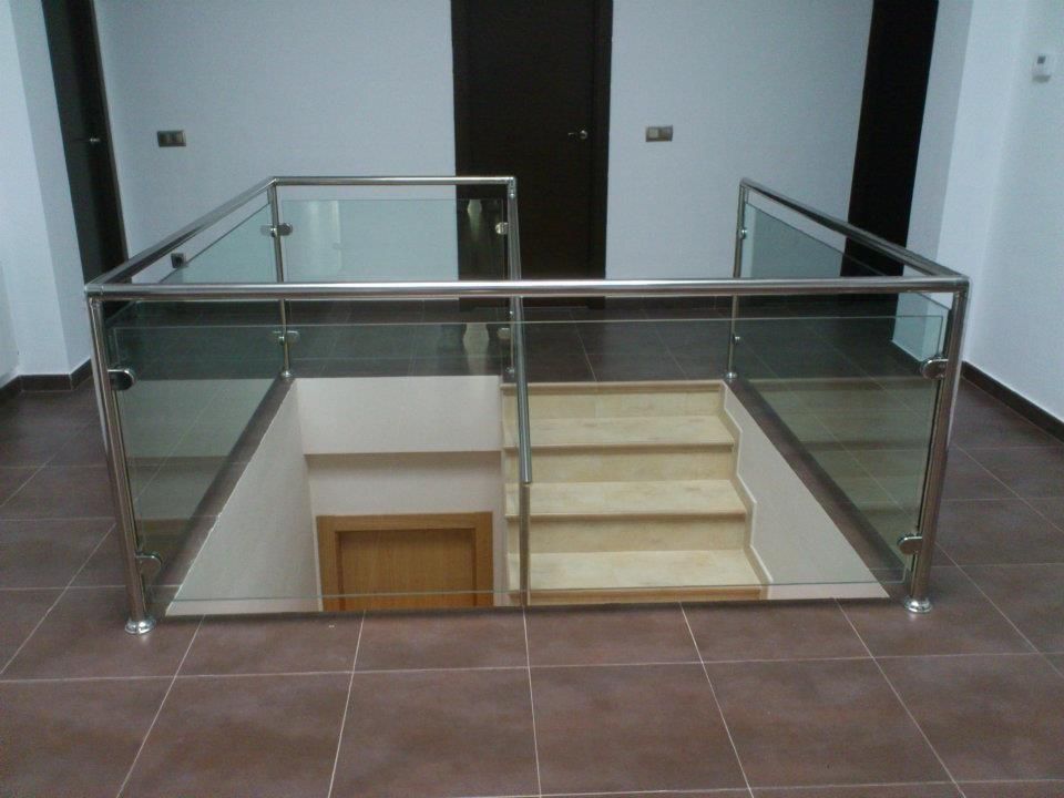 Escalera moderna con barandilla de cristal y estructura de acero inoxidable, suelo de baldosas de color marrón.