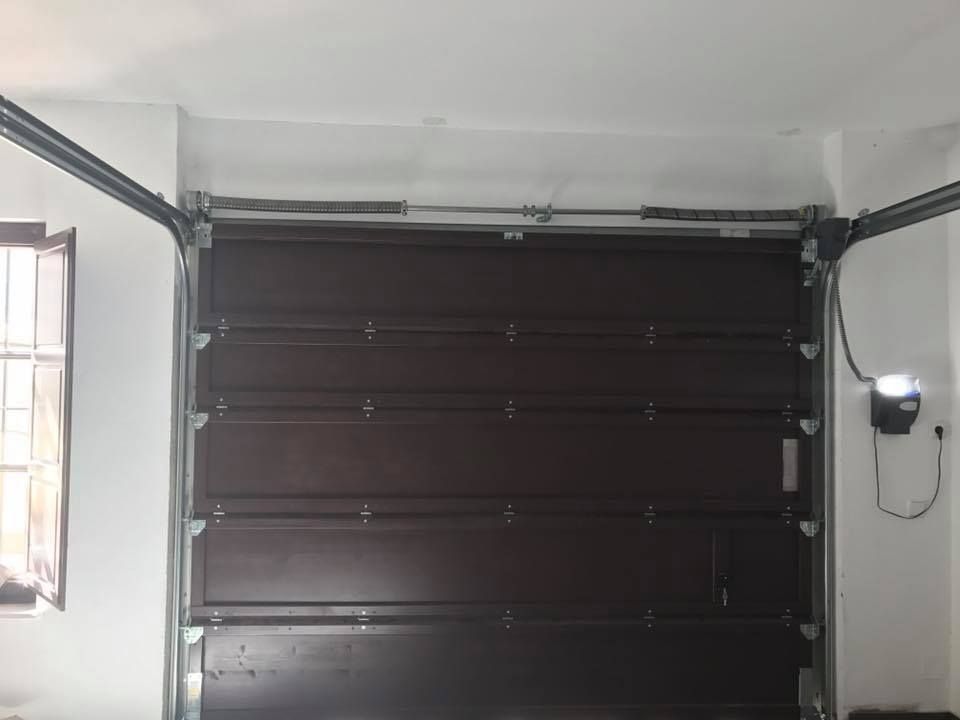 Puerta de garaje marrón, cerrada, con rieles metálicos y mecanismo de resorte, vista interior.