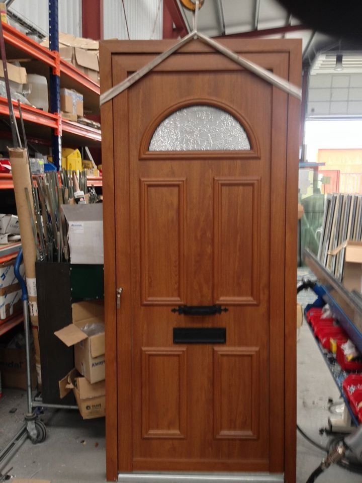 Puerta de entrada marrón con panel de vidrio arqueado, herrajes negros, dentro de un almacén.