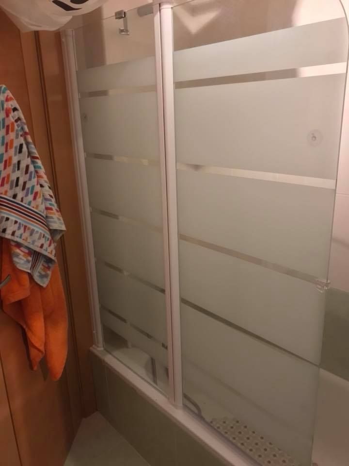 Mampara de ducha con paneles de cristal blanco esmerilado y toalla colgada en un gancho.