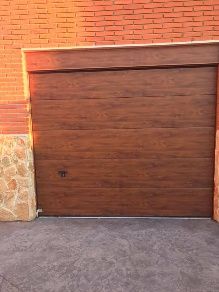 Puerta de garaje de madera marrón contra una pared de ladrillo. Entrada de hormigón al frente.