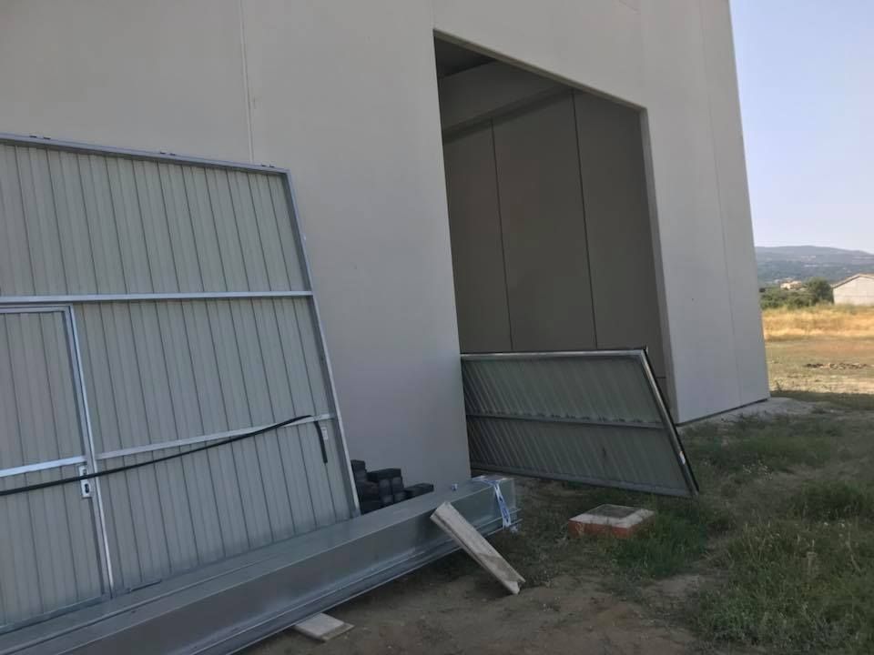 Edificio en construcción, con puerta abierta y portón metálico caído. Paredes grises y un luminoso exterior.
