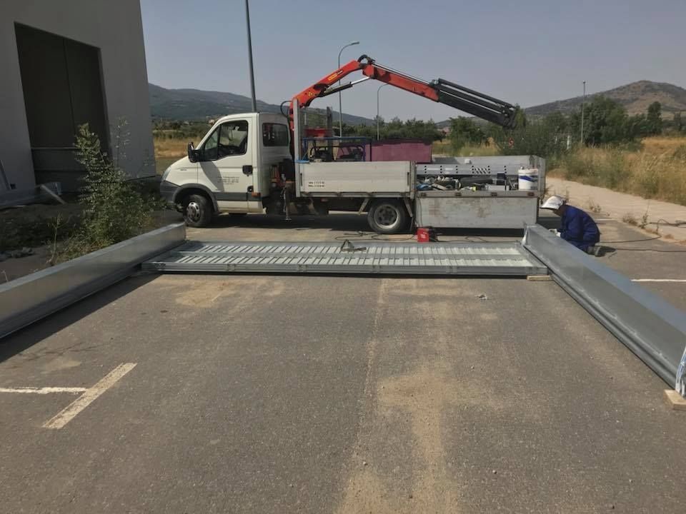 Camión con grúa descargando láminas metálicas en un estacionamiento en un día soleado.