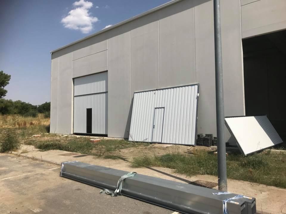 Exterior de un edificio industrial gris claro con puertas abiertas y cerradas y materiales metálicos desechados.