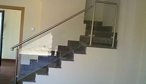 Escalera con pasamanos de acero inoxidable, escalones de granito y pared parcialmente pintada.