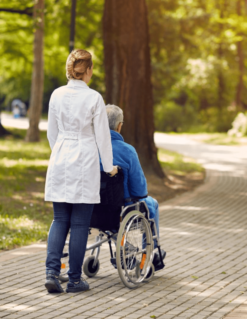 Person schiebt einen älteren Menschen im Rollstuhl