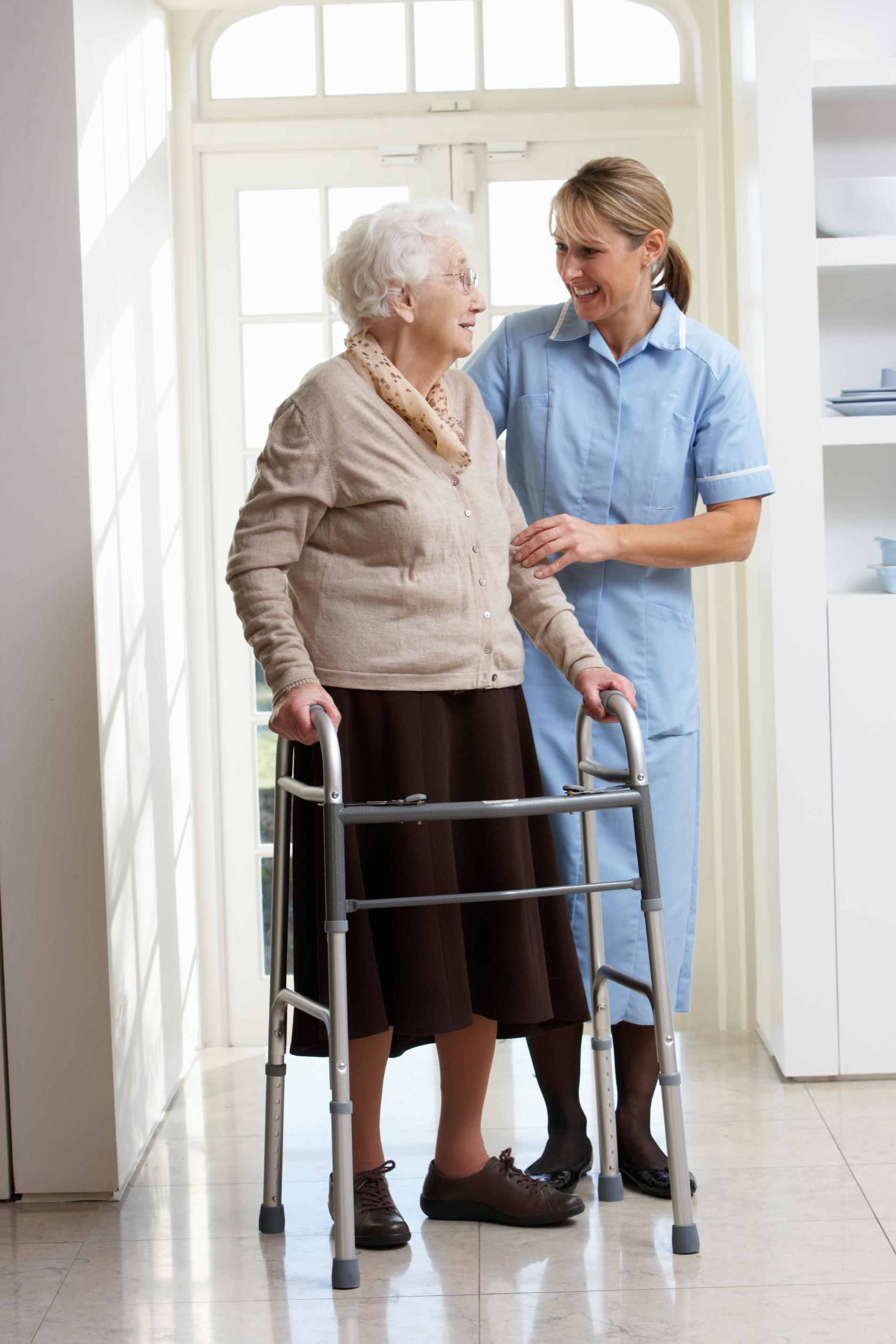 Pflegefachkraft unterstützt alte Person beim Gehen mit der Gehhilfe
