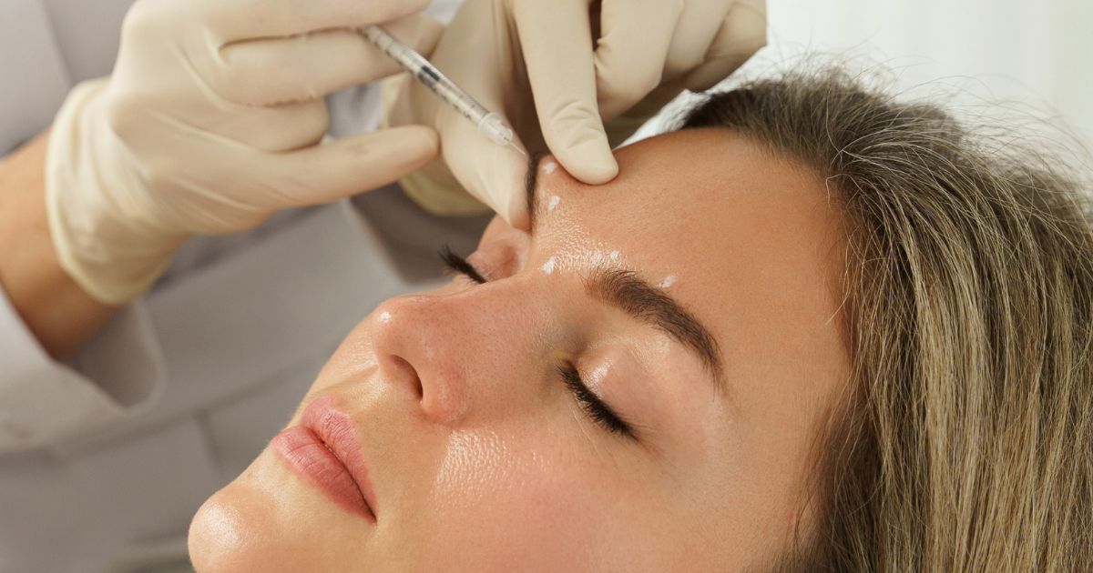 Pequeña oficina en casa con escritorio blanco, ventana y sofá gris.