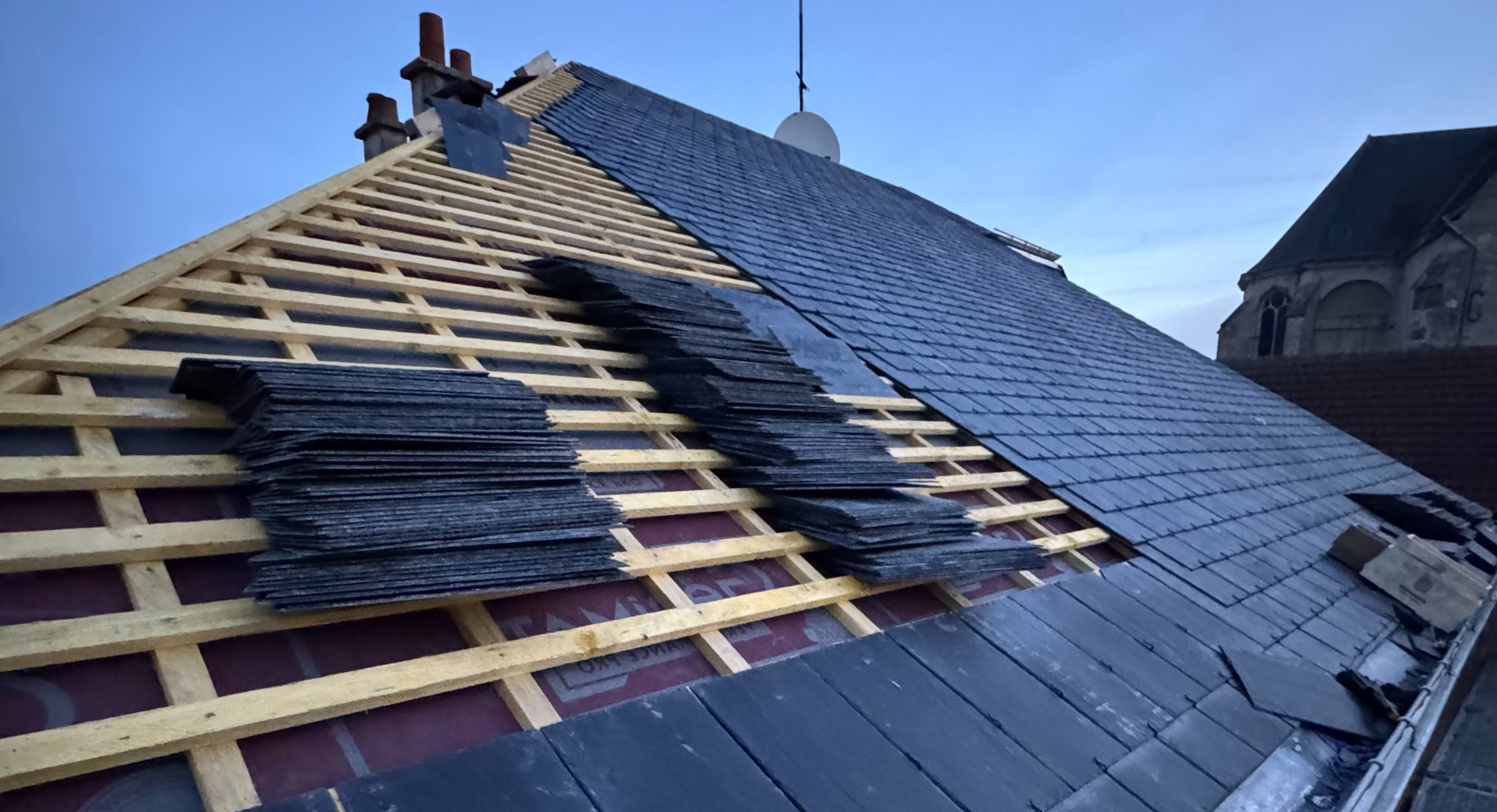 Un toit est en cours de construction avec des tuiles d'ardoise et des poutres en bois.