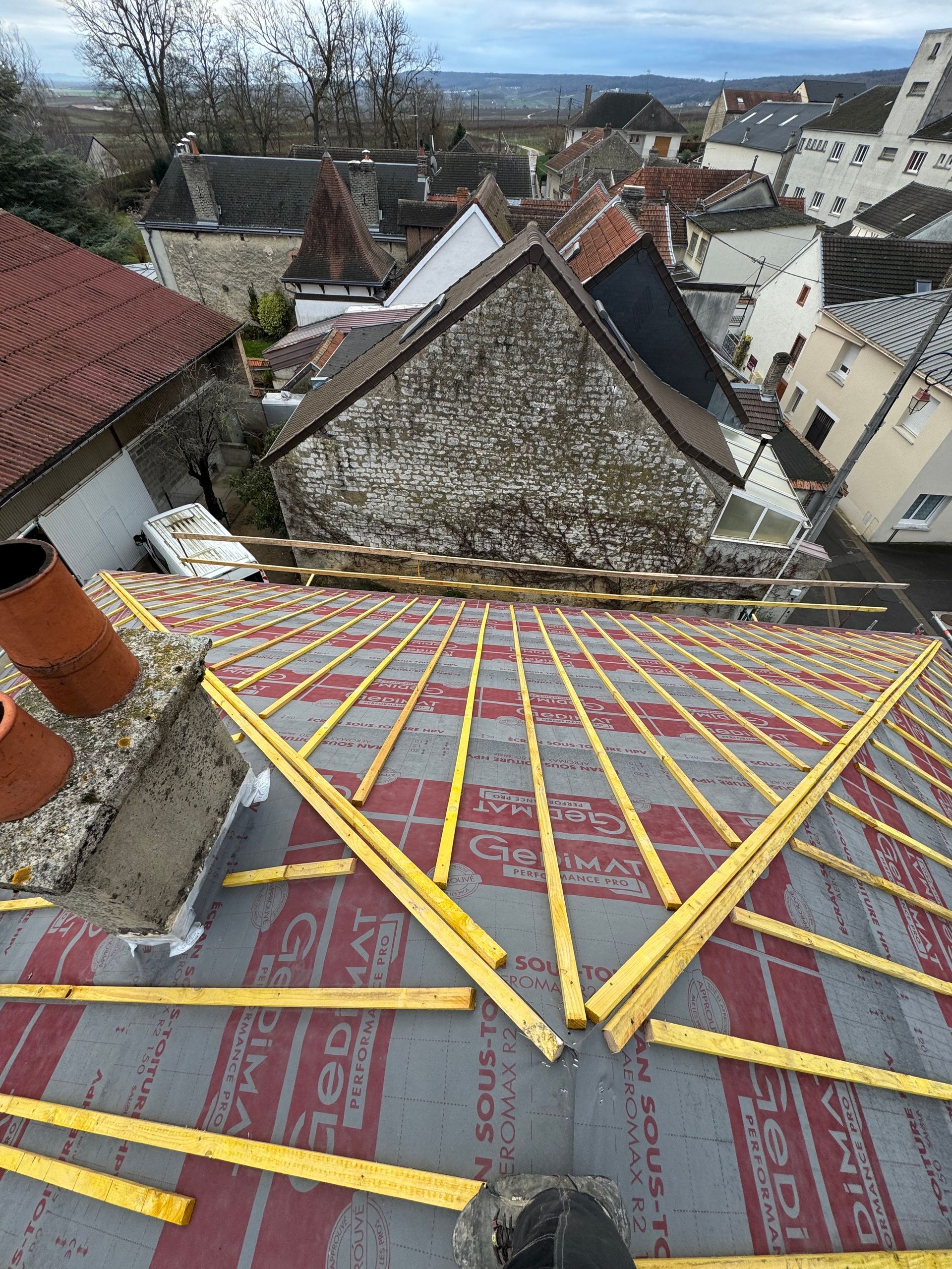 Un toit est en cours de construction avec des poutres en bois et des bardeaux.