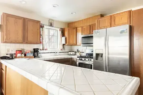 A kitchen with light wooden cabinets, white tile countertops, and stainless steel appliances.