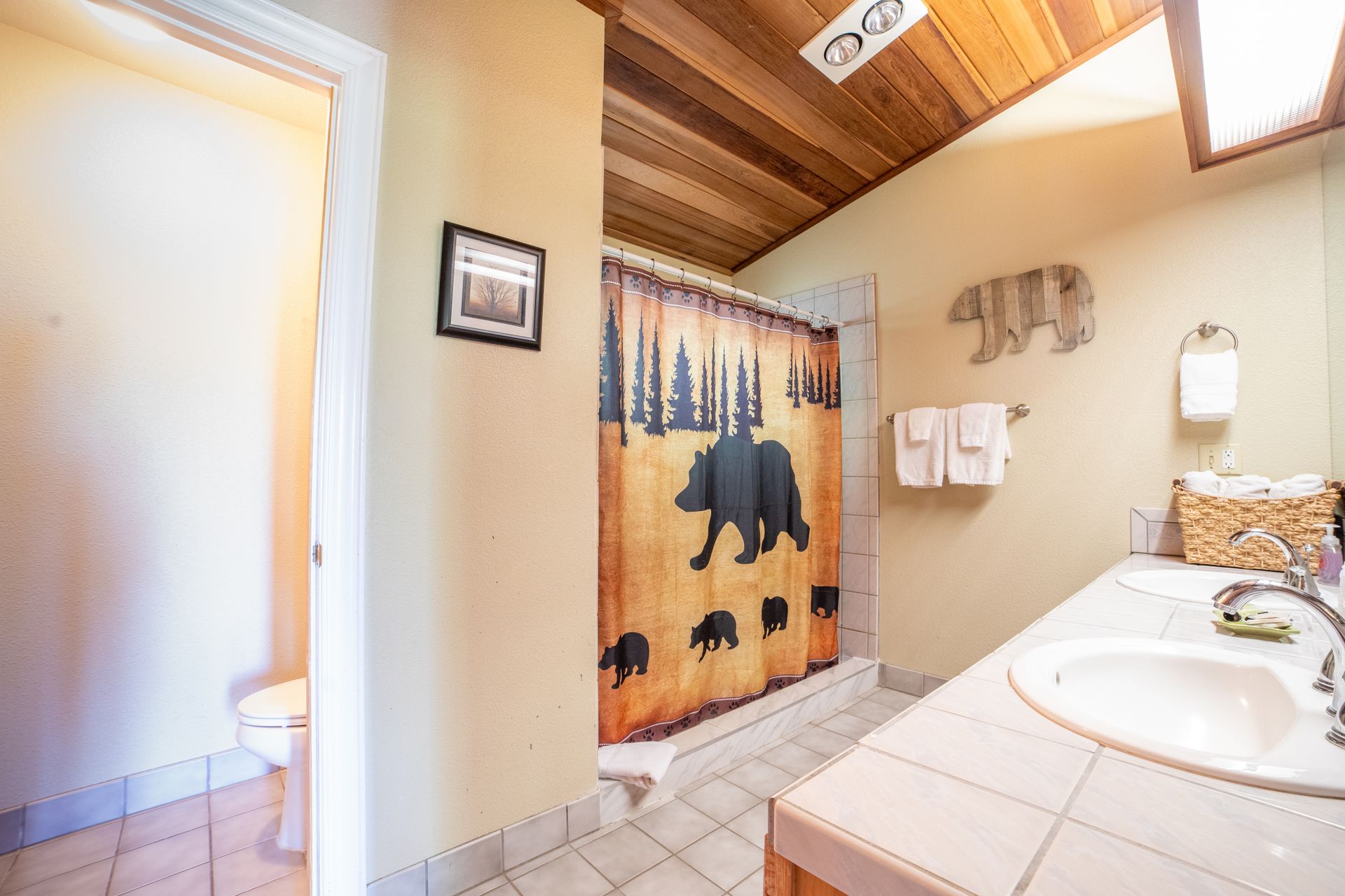 Bathroom with bear shower curtain, wooden bear art, and vanity.