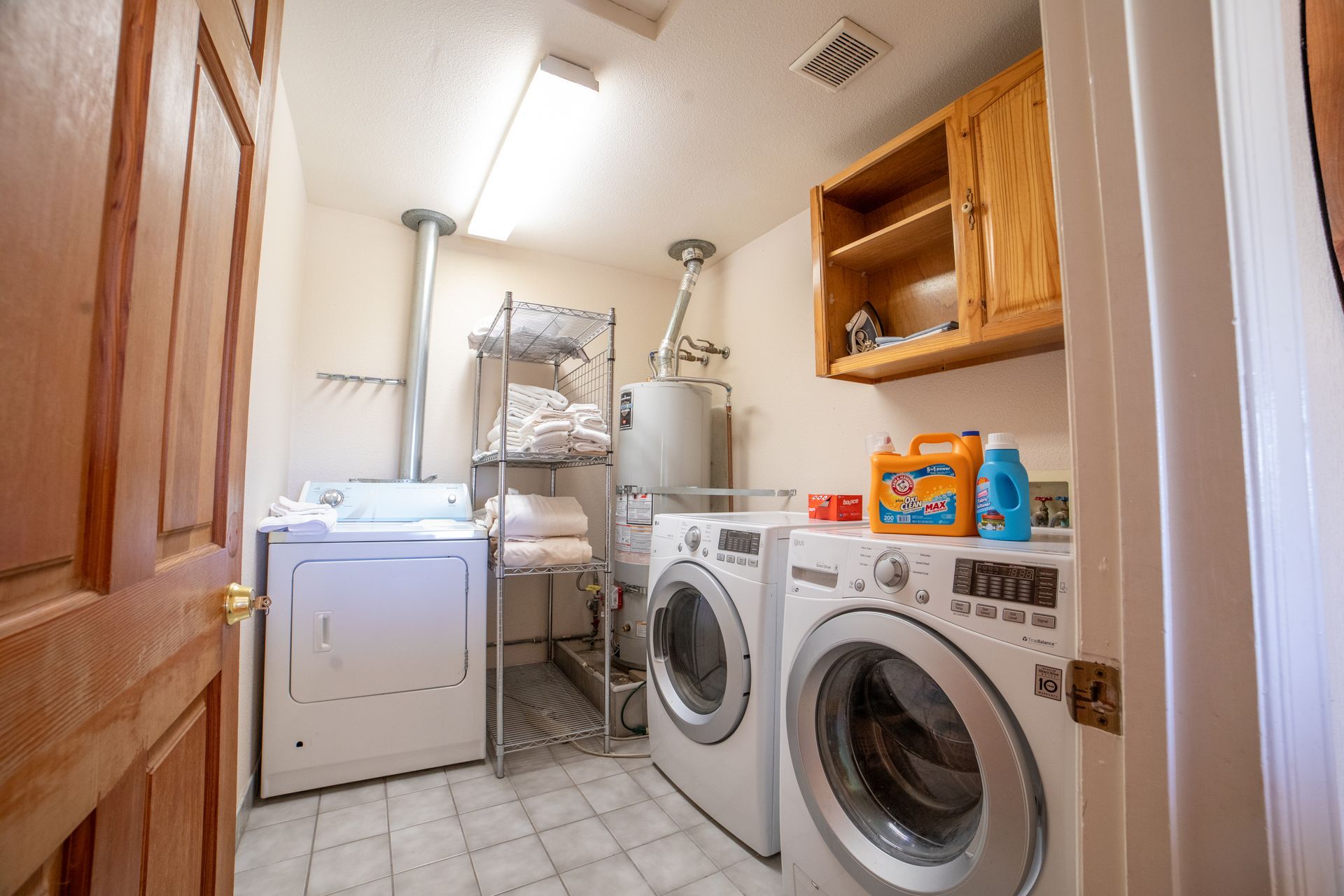 Laundry room with washer, dryer, water heater, and shelving. Cabinets and cleaning supplies are visible.