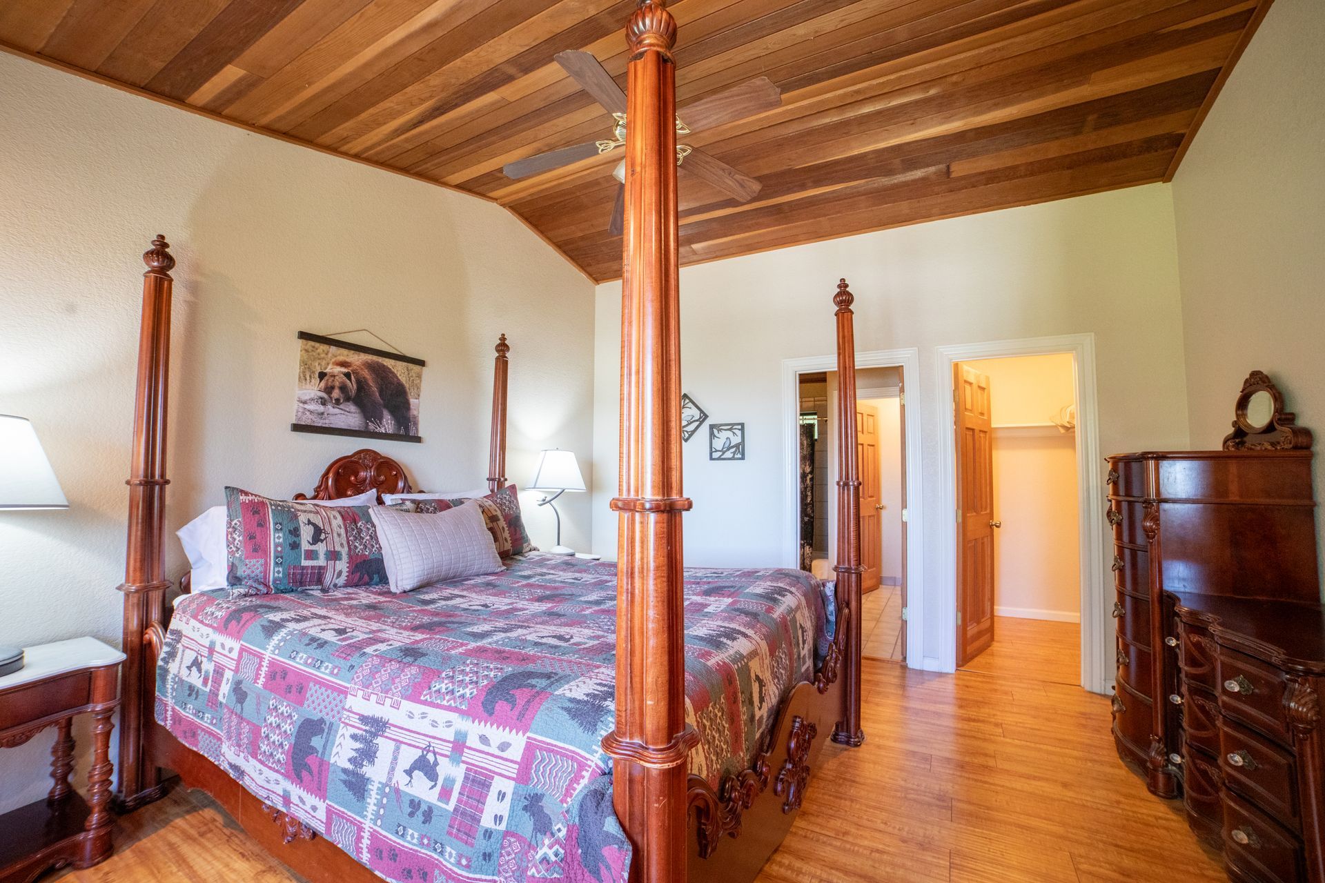 Bedroom with a four-poster bed, wooden ceiling and floor, and a dresser.