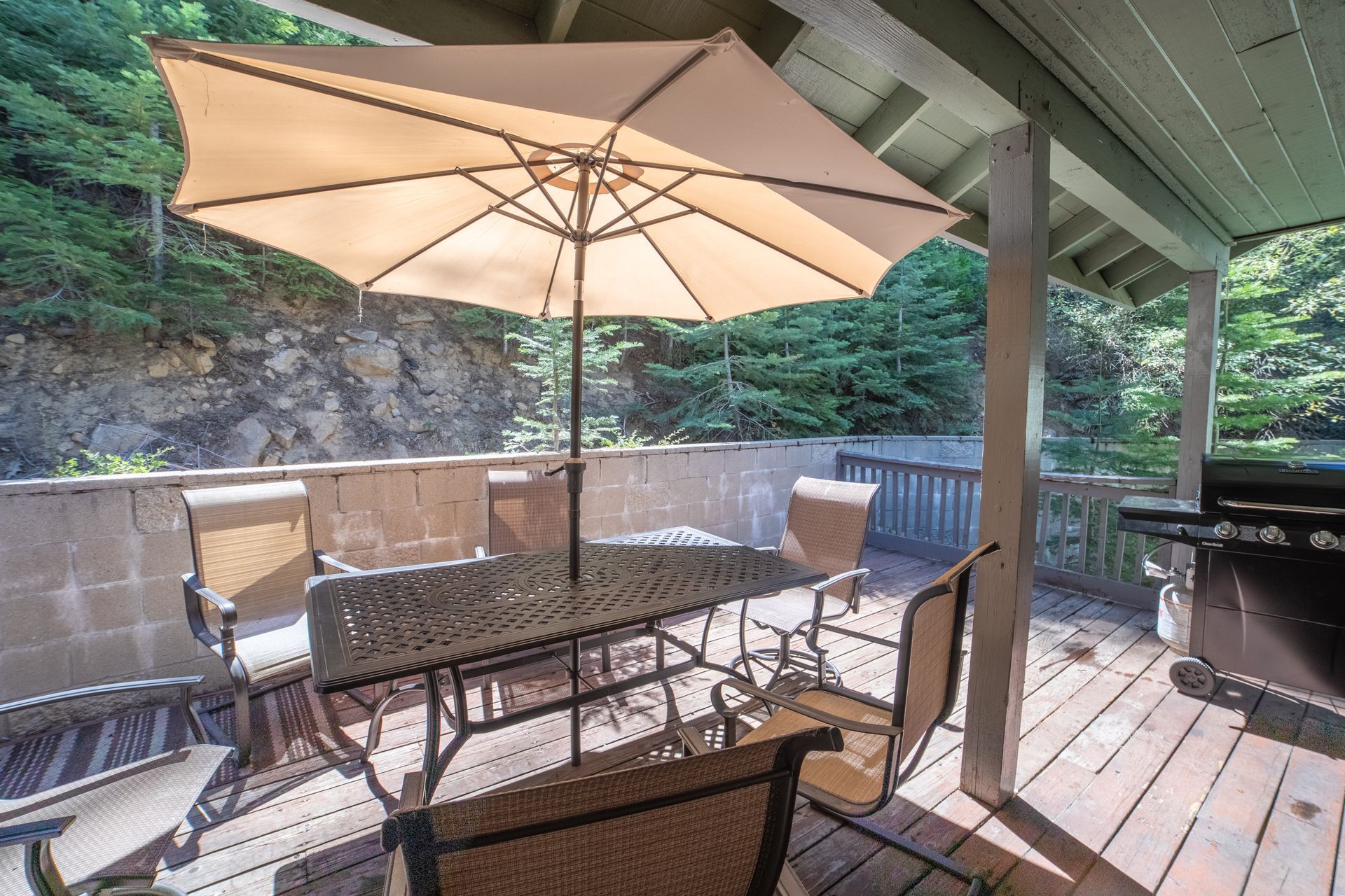 Outdoor patio with table, chairs, umbrella, and grill, surrounded by trees.
