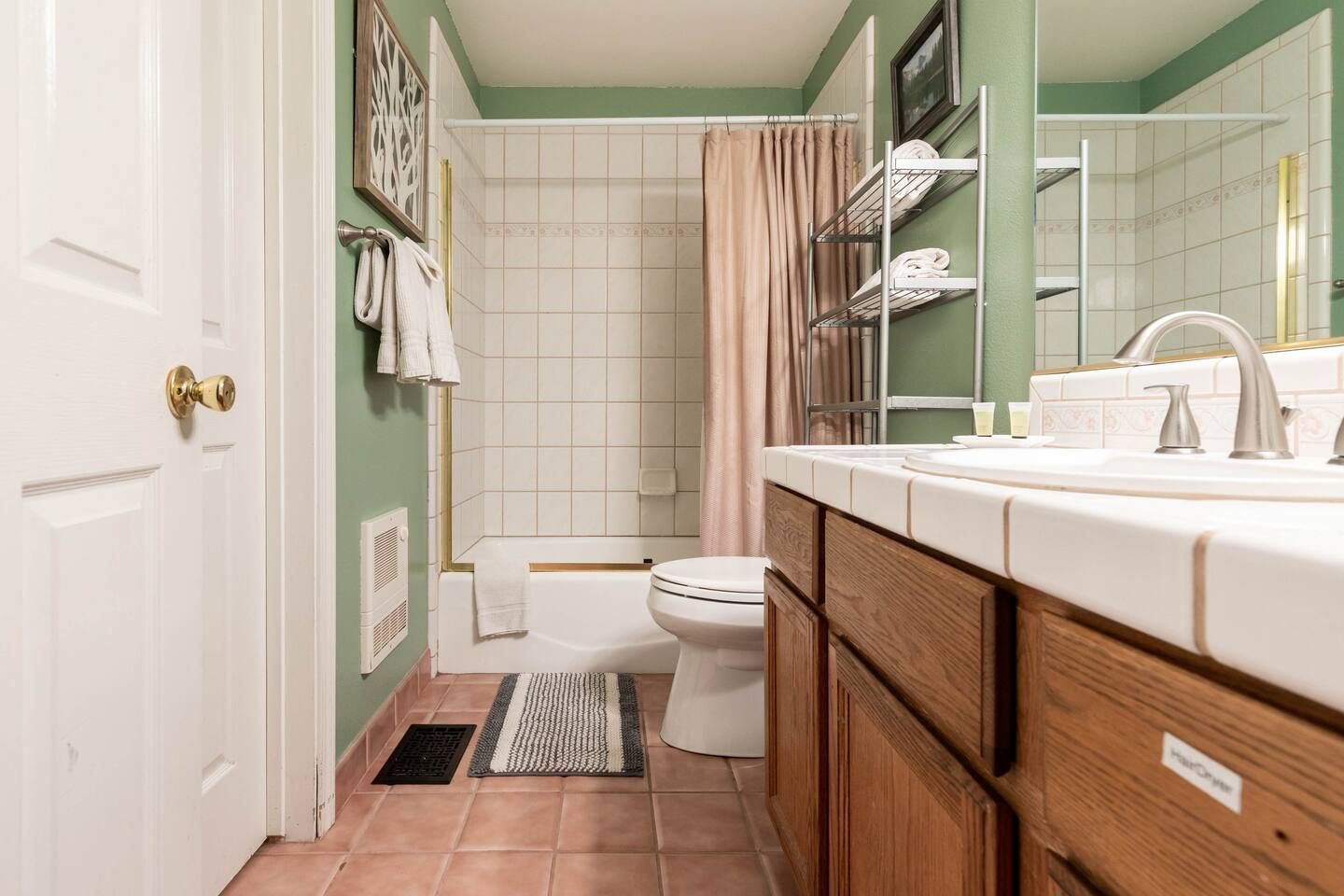 Bathroom with pink tile floor, green walls, white tub, and wooden vanity.
