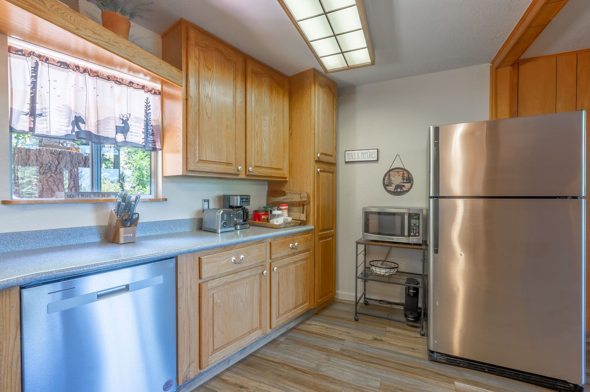 Kitchen with wood cabinets, stainless steel appliances, and a window with a curtain.