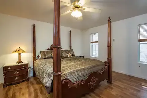 A bedroom with a four-poster bed, wooden floors, and a nightstand with a lamp.