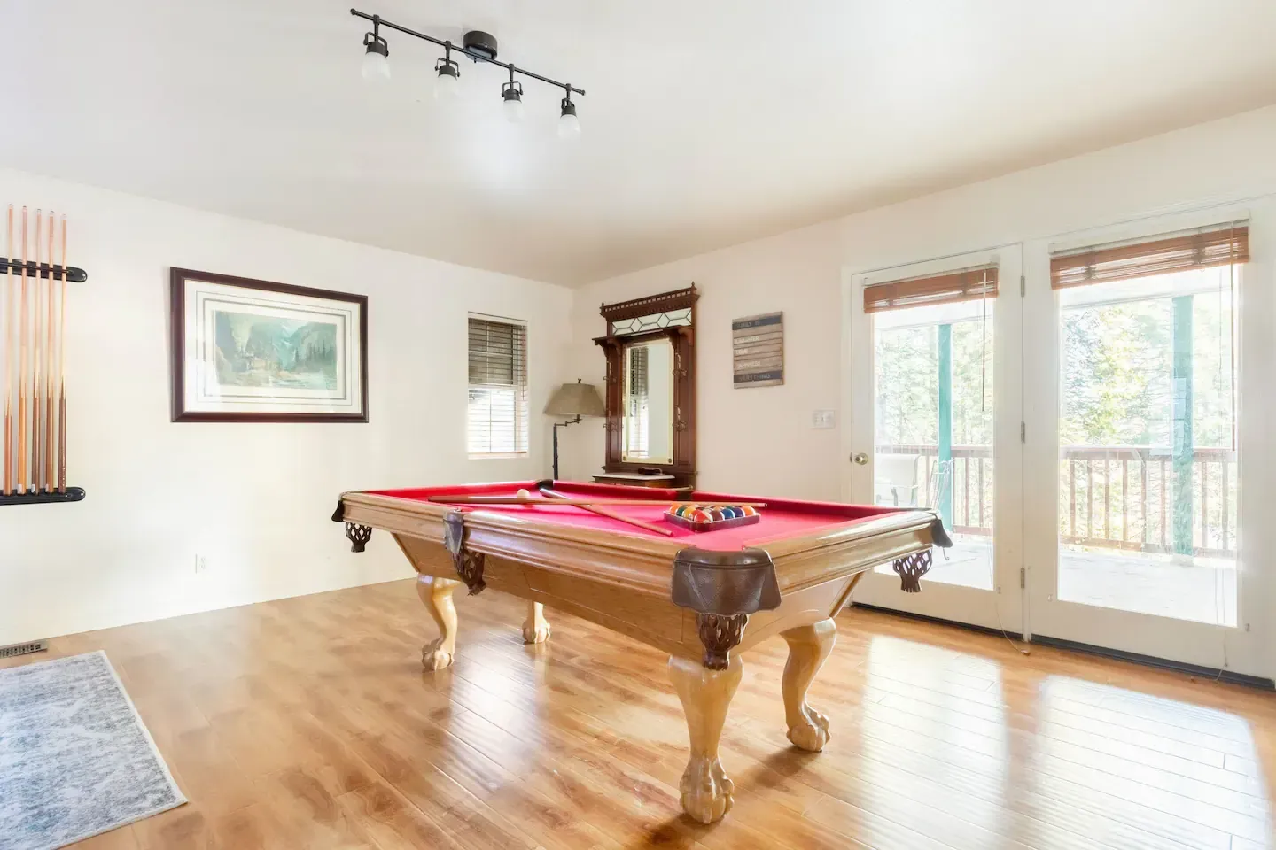 Pool table in a room with wood floors and large windows. Cue sticks and balls are present.