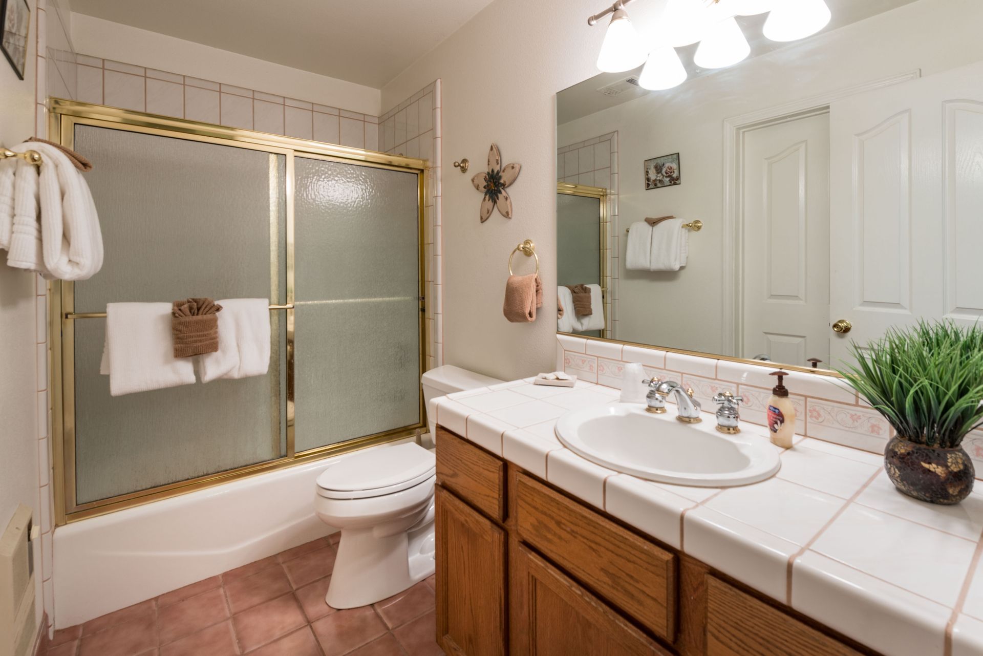 Bathroom with shower, toilet, and vanity. Light-colored walls, gold trim, and pink tile.