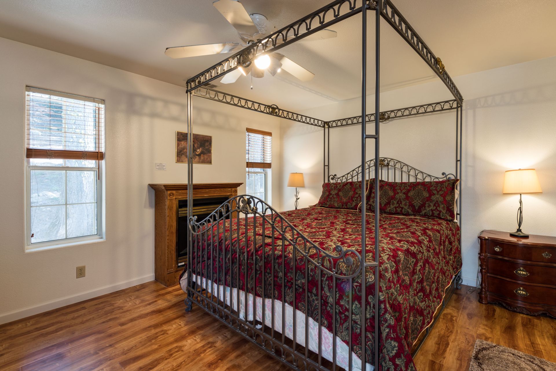 Bedroom with four-poster bed, fireplace, wood floors, and red patterned bedding.