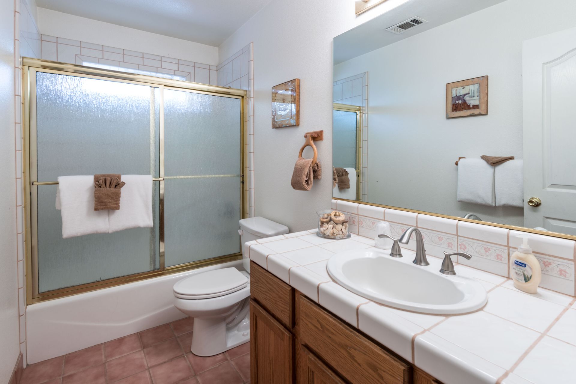 Bathroom with white sink, toilet, and bathtub. Brown cabinets and gold-framed shower door.