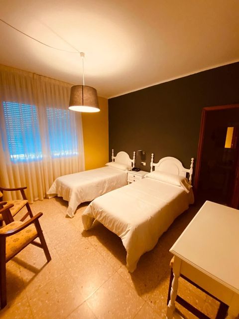 Un dormitorio acogedor con dos camas individuales, iluminación cálida, una ventana con cortinas y una silla de madera.