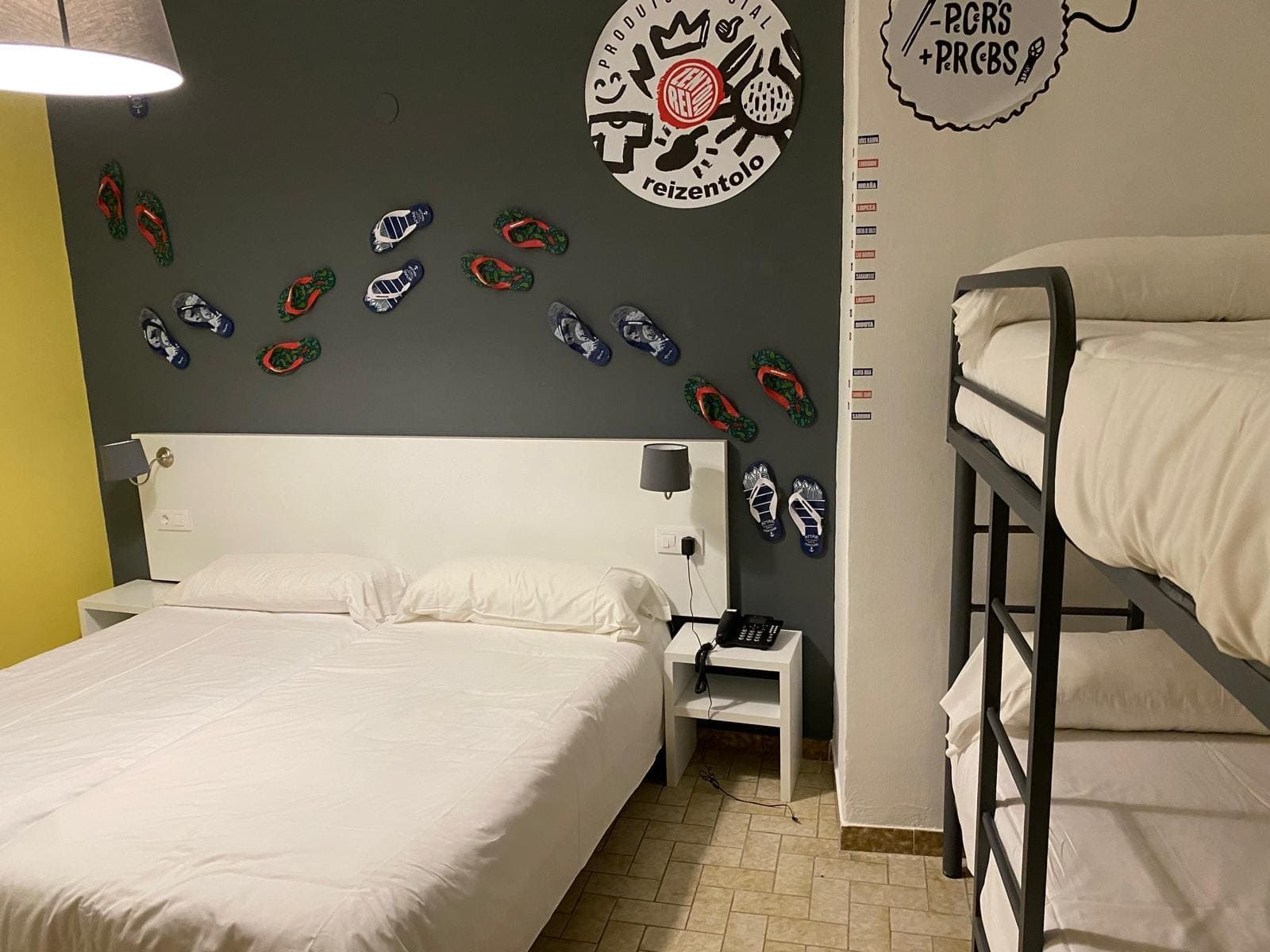 Habitación compartida con dos camas, ropa de cama blanca y una pared decorativa oscura adornada con pegatinas de colores.