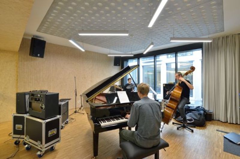 Un homme joue du piano dans une pièce avec d'autres personnes qui jouent des instruments.