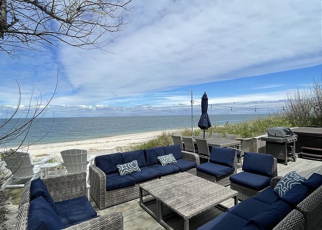 A patio with a couch , chairs , table and umbrella overlooking the ocean.